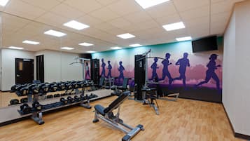 Een fitnessruimte met diverse trainingsapparaten, een muurschildering van hardlopers en een aan de muur bevestigde televisie.