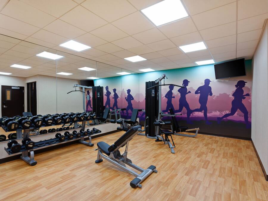 Een fitnessruimte met diverse trainingsapparaten, een muurschildering van hardlopers en een aan de muur bevestigde televisie.