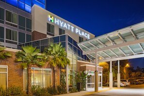 A Hyatt Place hotel with a modern glass facade, a covered entrance, and a parking area.