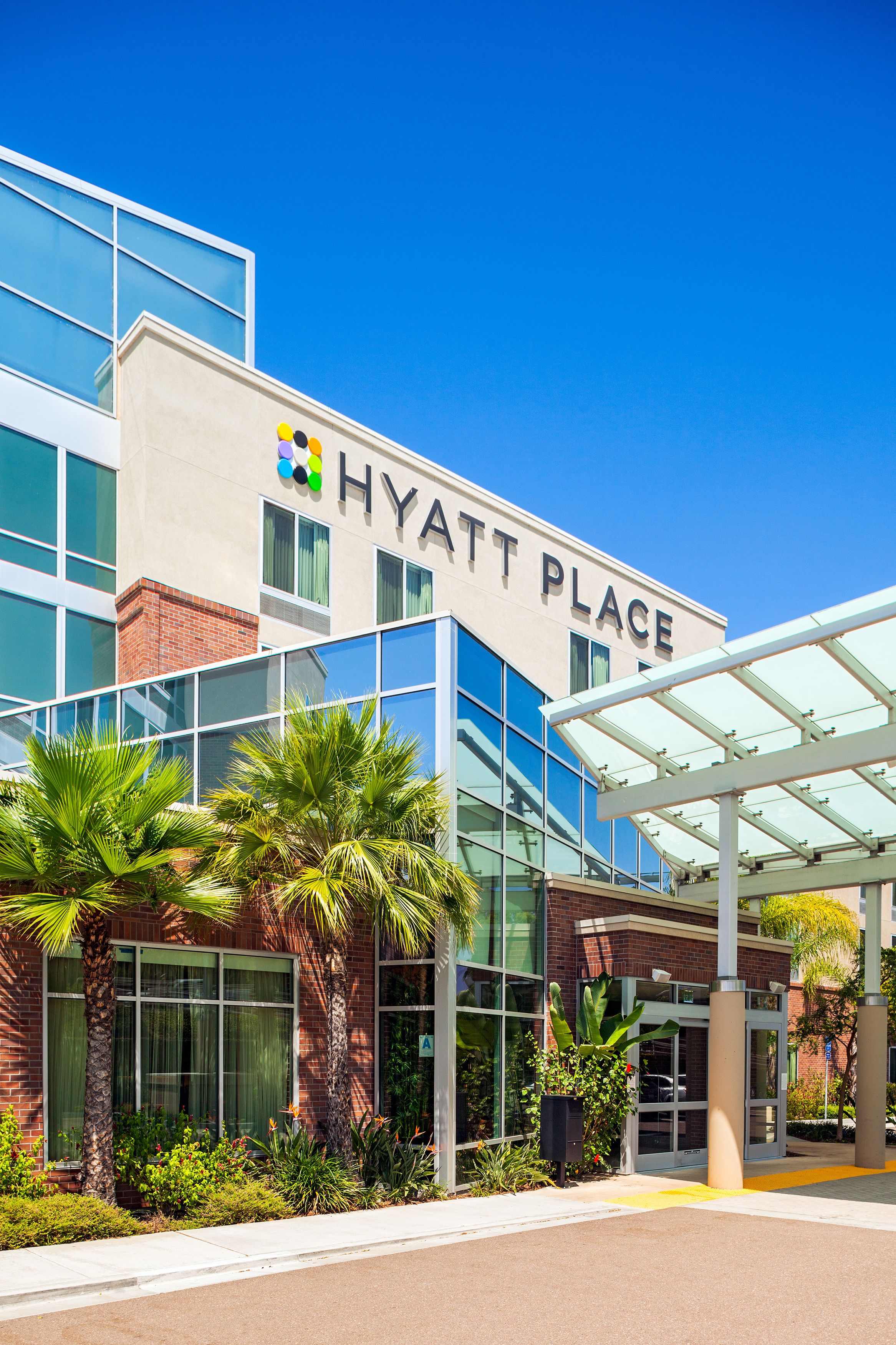 A modern Hyatt Place hotel with a glass facade, palm trees, and a covered entrance.