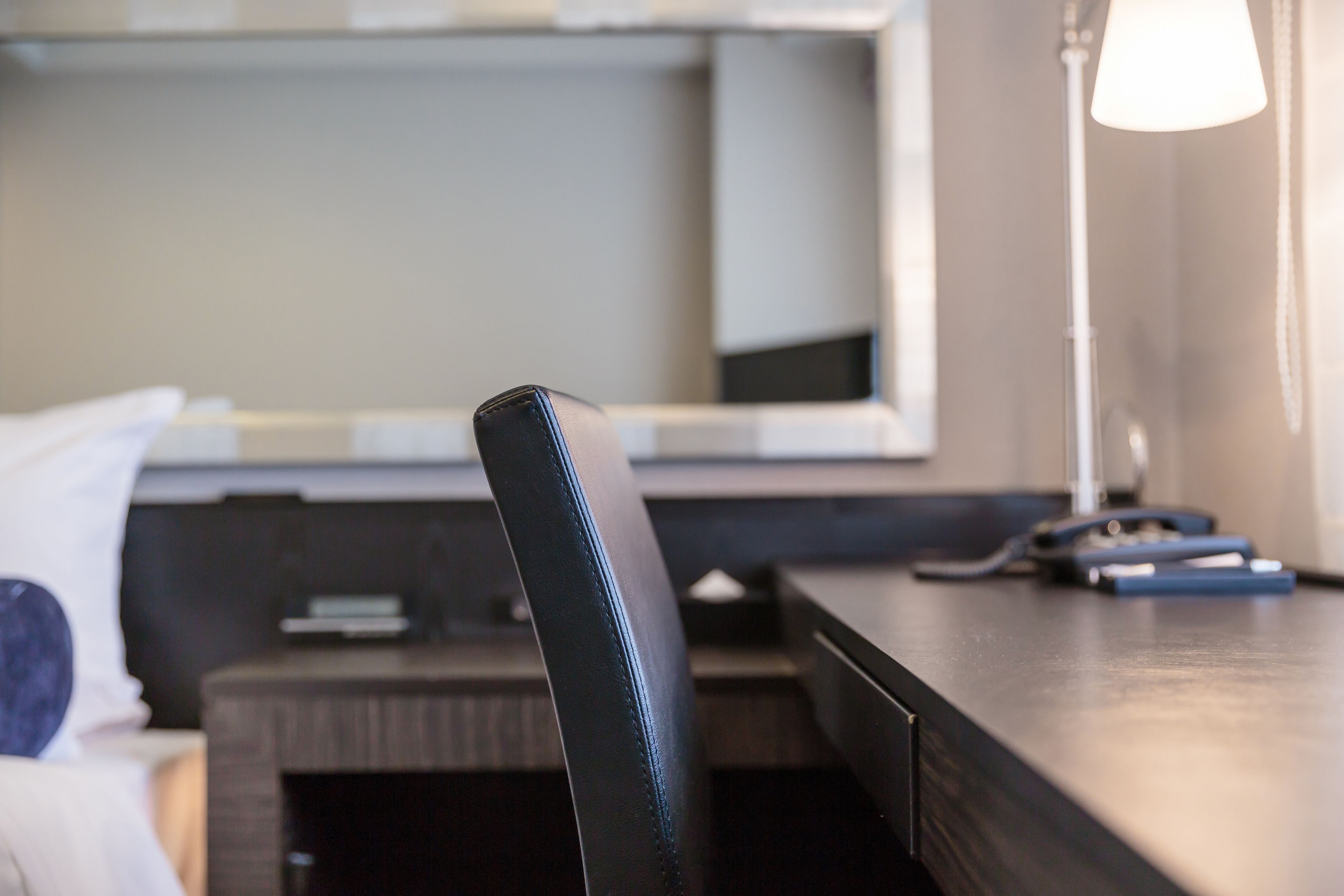 A hotel room with a desk, a chair, a lamp, and a mirror.