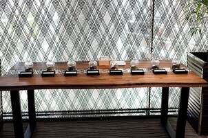A wooden table with glass jars and black boxes, set against a patterned metal fence.