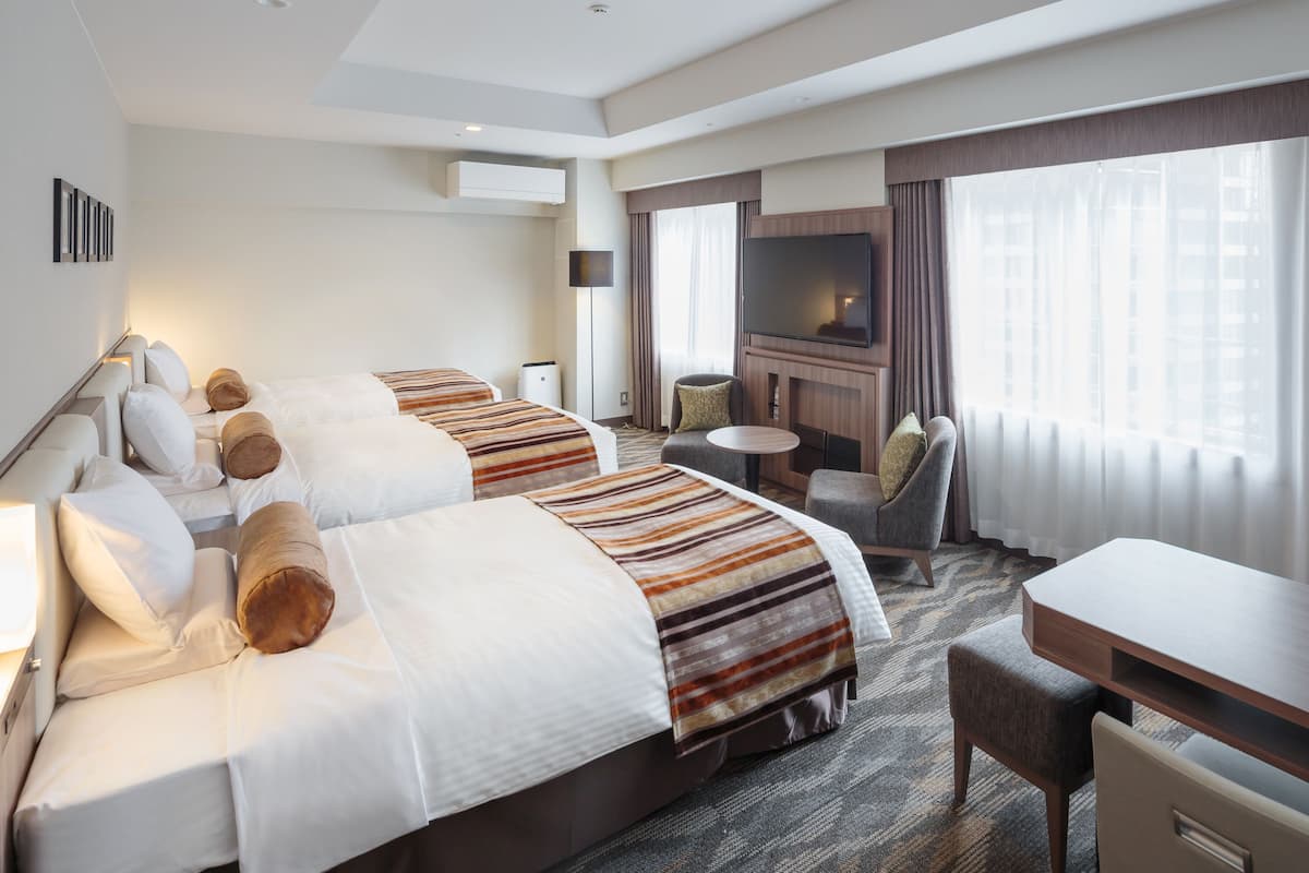 A hotel room with two beds, a TV, a desk, and a chair.