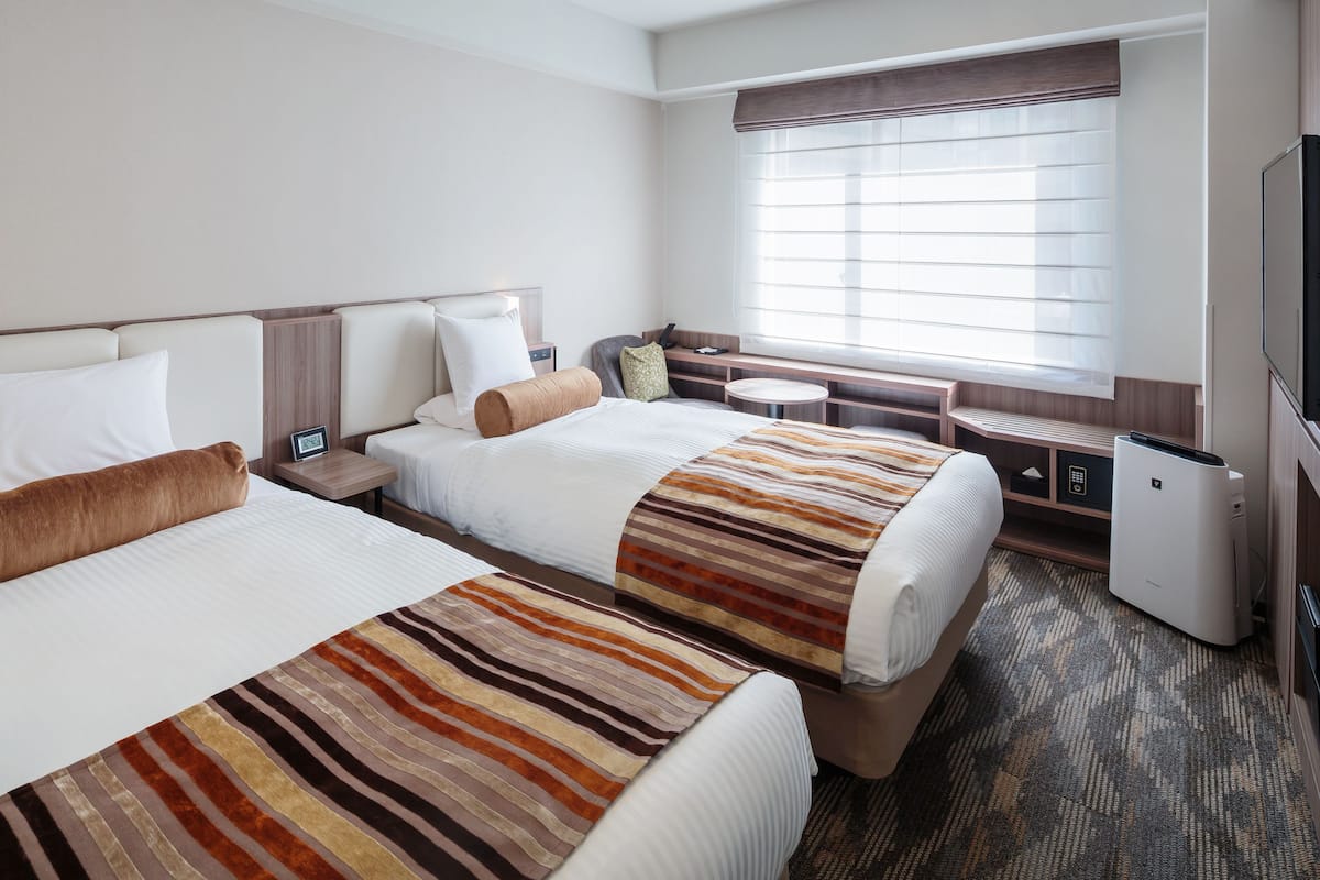 A hotel room with two beds, a seating area, a television, and a minibar.