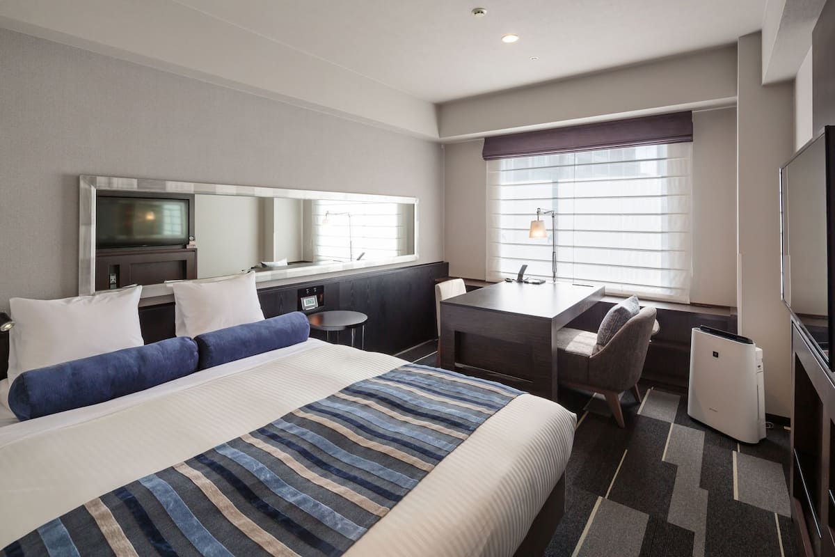 A hotel room with a bed, desk, chair, and a television.