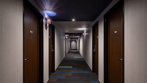 Un couloir d’hôtel avec des portes en bois numérotées 807 et 818, une moquette à motifs et des luminaires encastrés dans le plafond.
