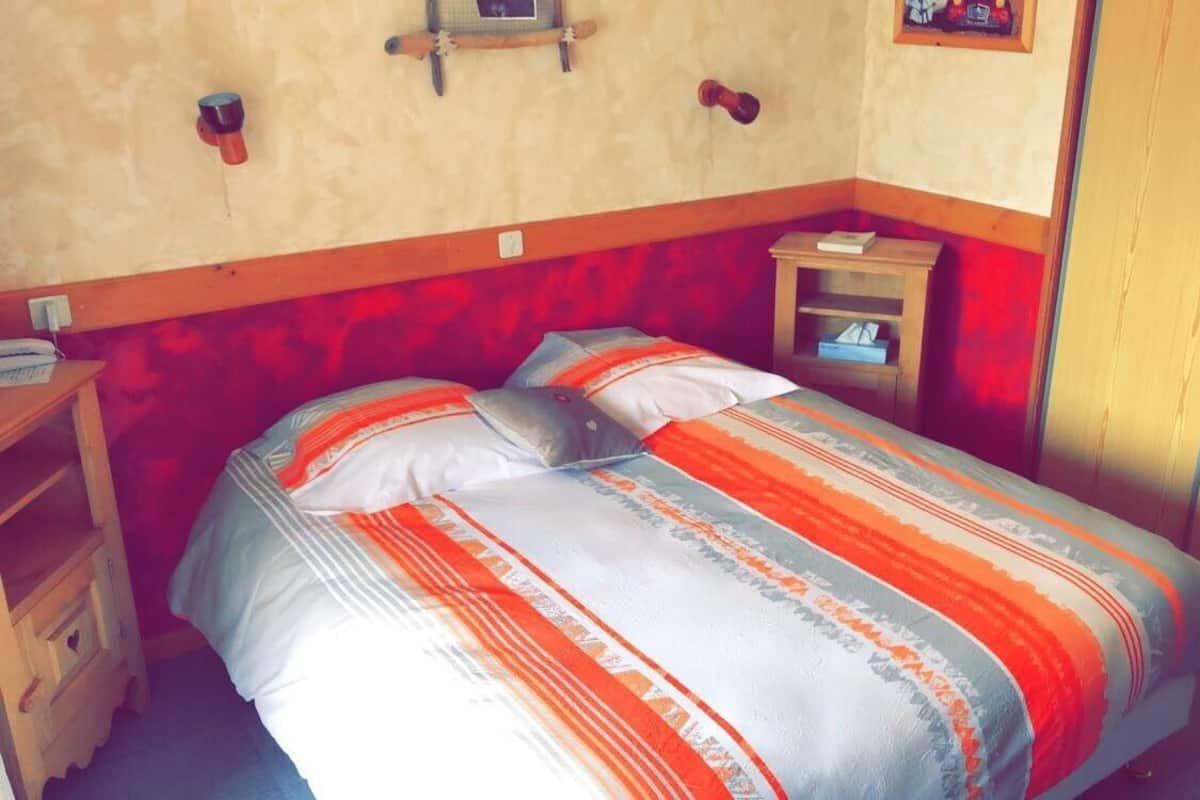 Una habitación con cama, mesita de noche de madera, una pequeña mesa y un armario.