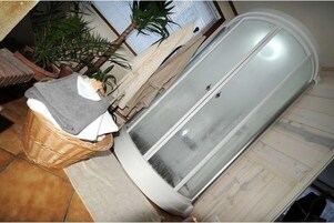 Una habitación con una bañera metálica grande y curvada, una cesta de mimbre con ropa y una planta en maceta.