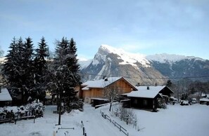 Een besneeuwd dorpje met houten huizen, een berg op de achtergrond en een heldere lucht.
