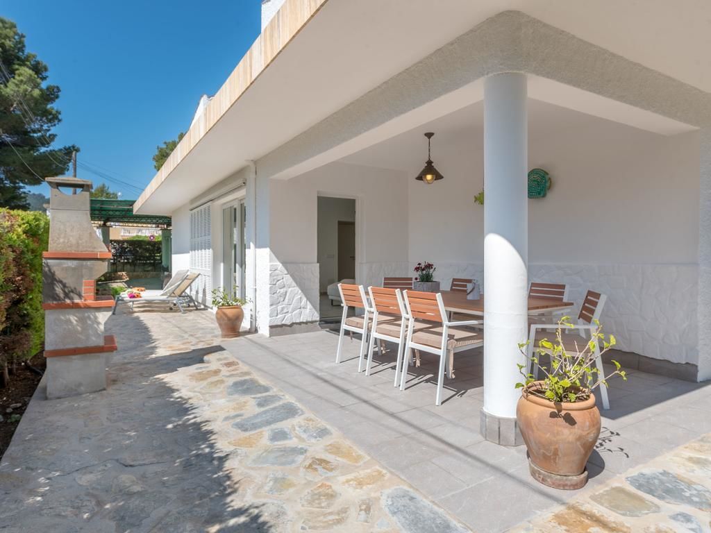 An outdoor patio with a stone floor, white columns, a dining table with chairs, and potted plants.