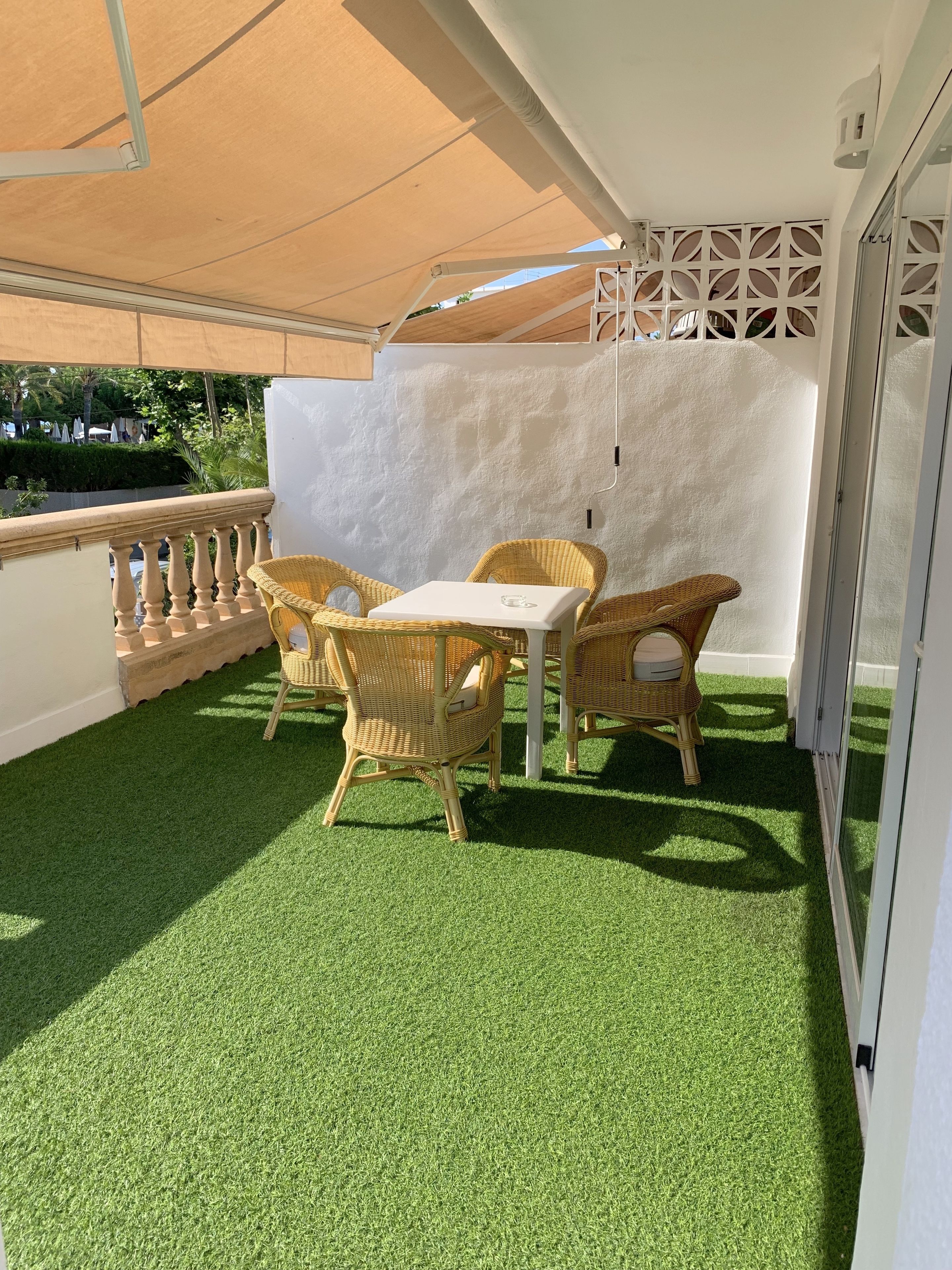 A balcony with artificial grass, wicker furniture, and a white partition.