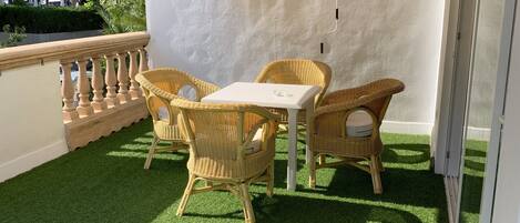 A balcony with artificial grass, wicker furniture, and a white partition.