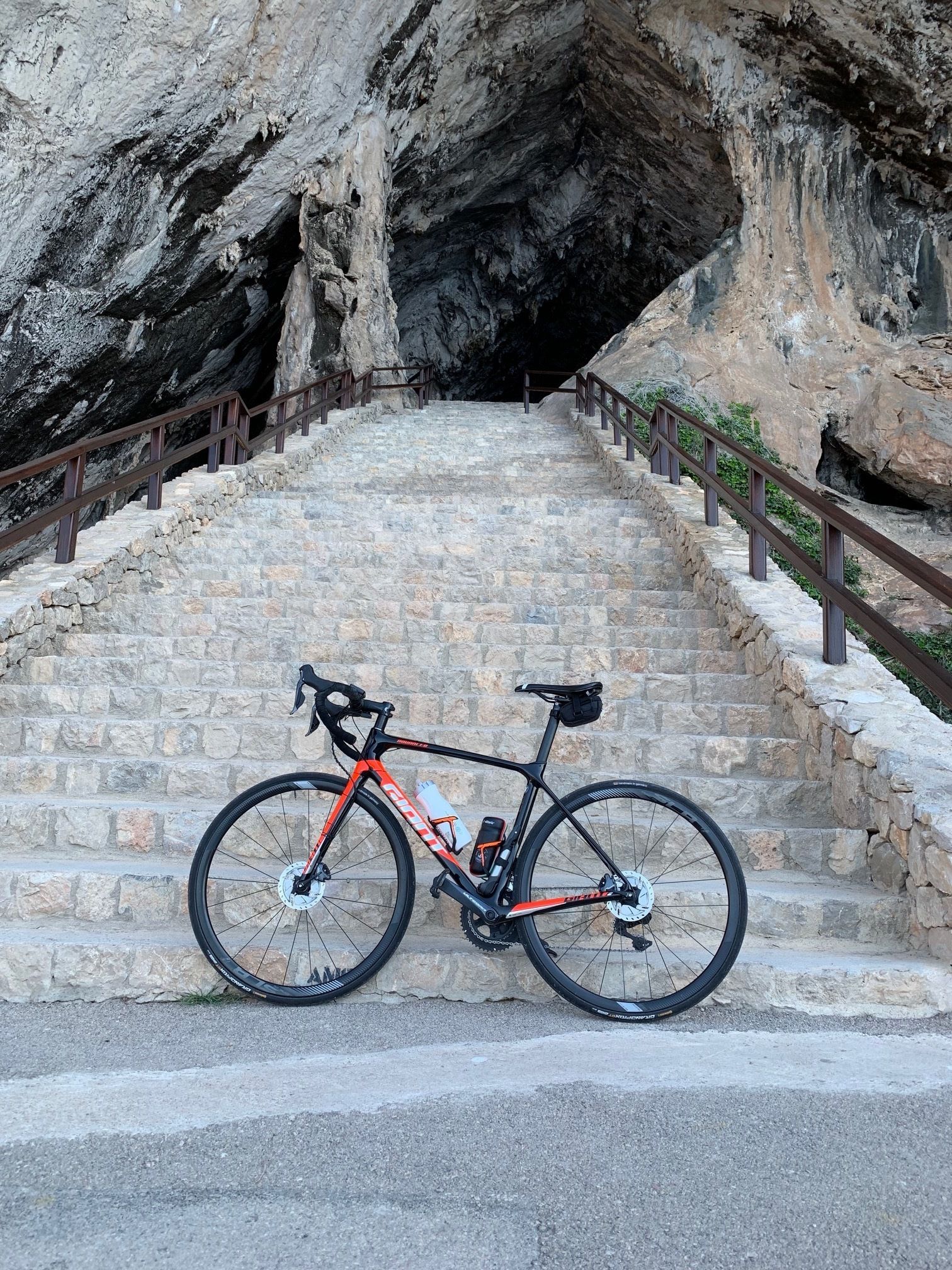 Un vélo est garé sur des marches en pierre, bordées de rampes en bois, qui mènent à une zone rocheuse.