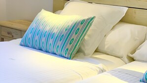 Een netjes opgemaakt bed met witte lakens, een kussen met een groen-wit patroon, en een enkele rode bloem op een witte handdoek.