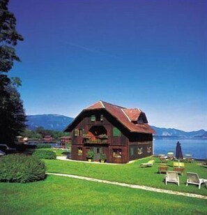 Una casa di legno rustica con tetto spiovente, un balcone e vista su un lago e montagne sullo sfondo.