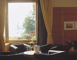 Een kamer met een groot raam, een tafel met glazen en een karaf, en twee fauteuils.