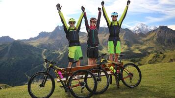 Trois personnes sont debout sur un banc, à côté de leurs vélos, et contemplent un paysage montagneux.