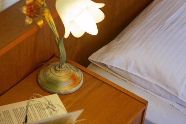 Una mesita de noche con una lámpara, un libro y un almohadón sobre un tablero de madera.