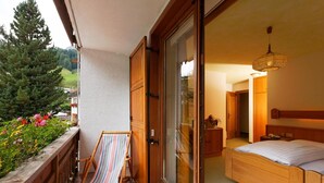 Ein Balkon mit einem Holzstuhl, einem Bett mit Holz-Kopfteil und Blick auf einen bewaldeten Bereich.