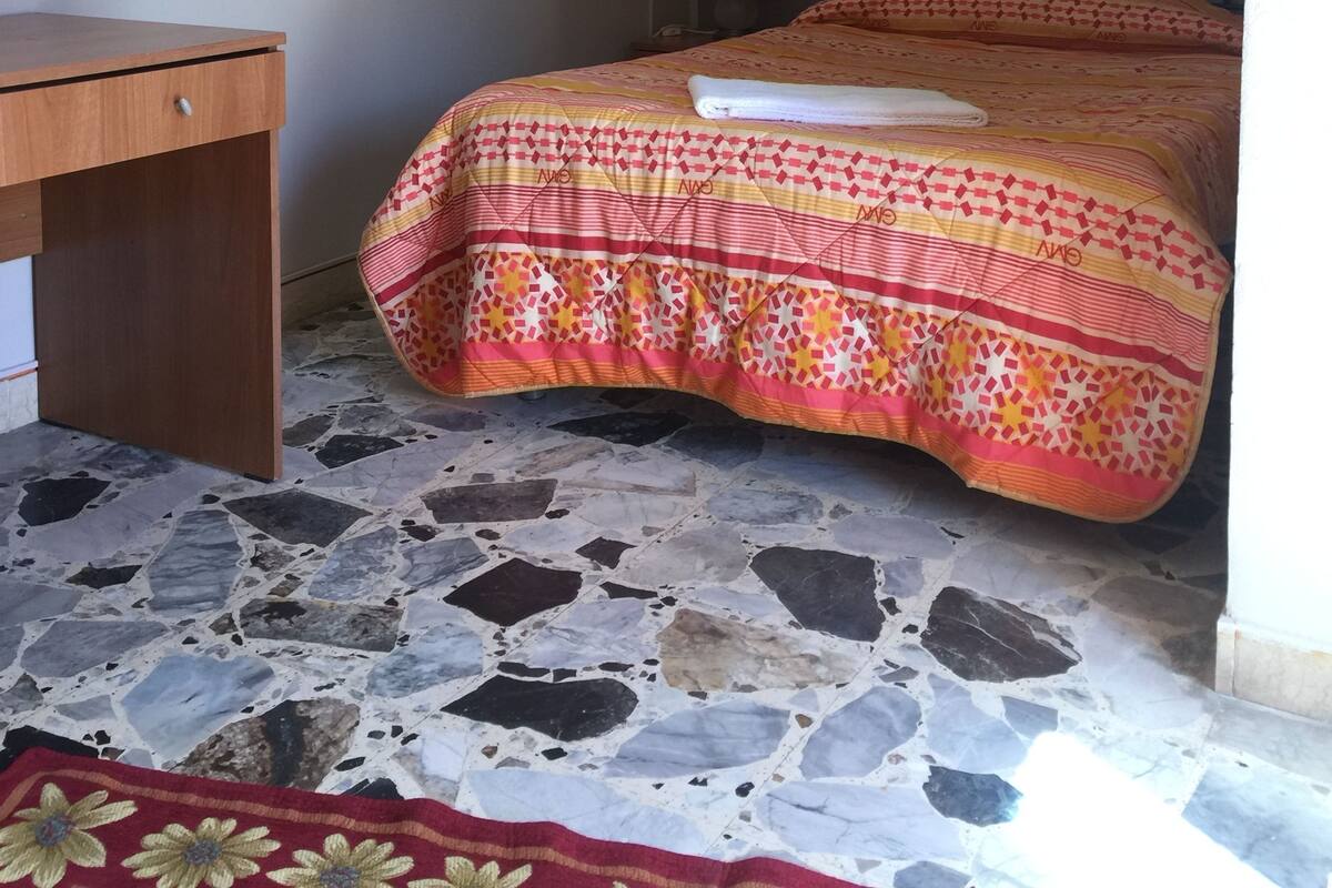 A bedroom with a bed, a desk, a TV, and a painting on the wall.