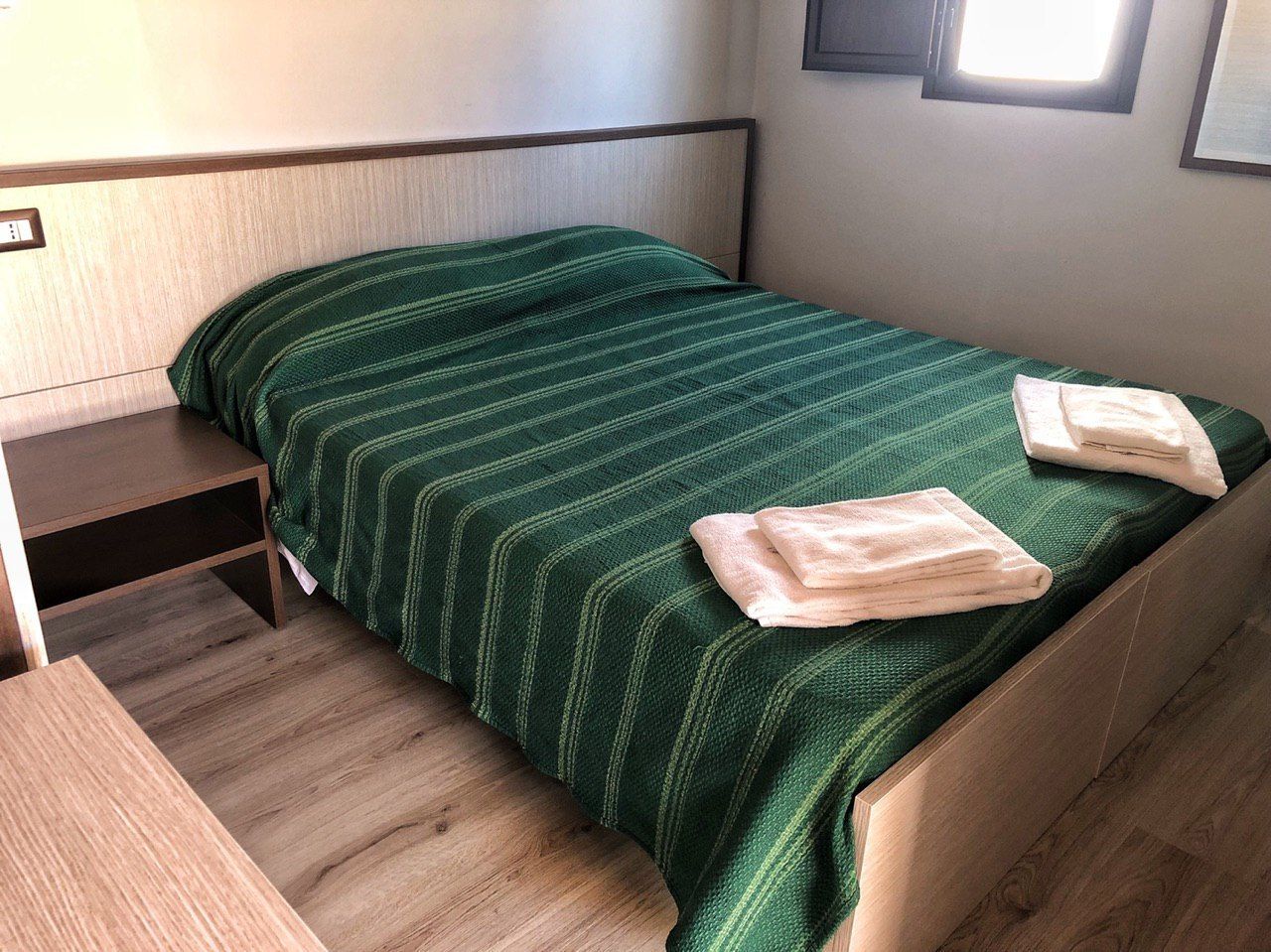 Une petite chambre avec un lit simple, une tête de lit en bois, une table de chevet en bois et une couvre-lit à rayures vertes.