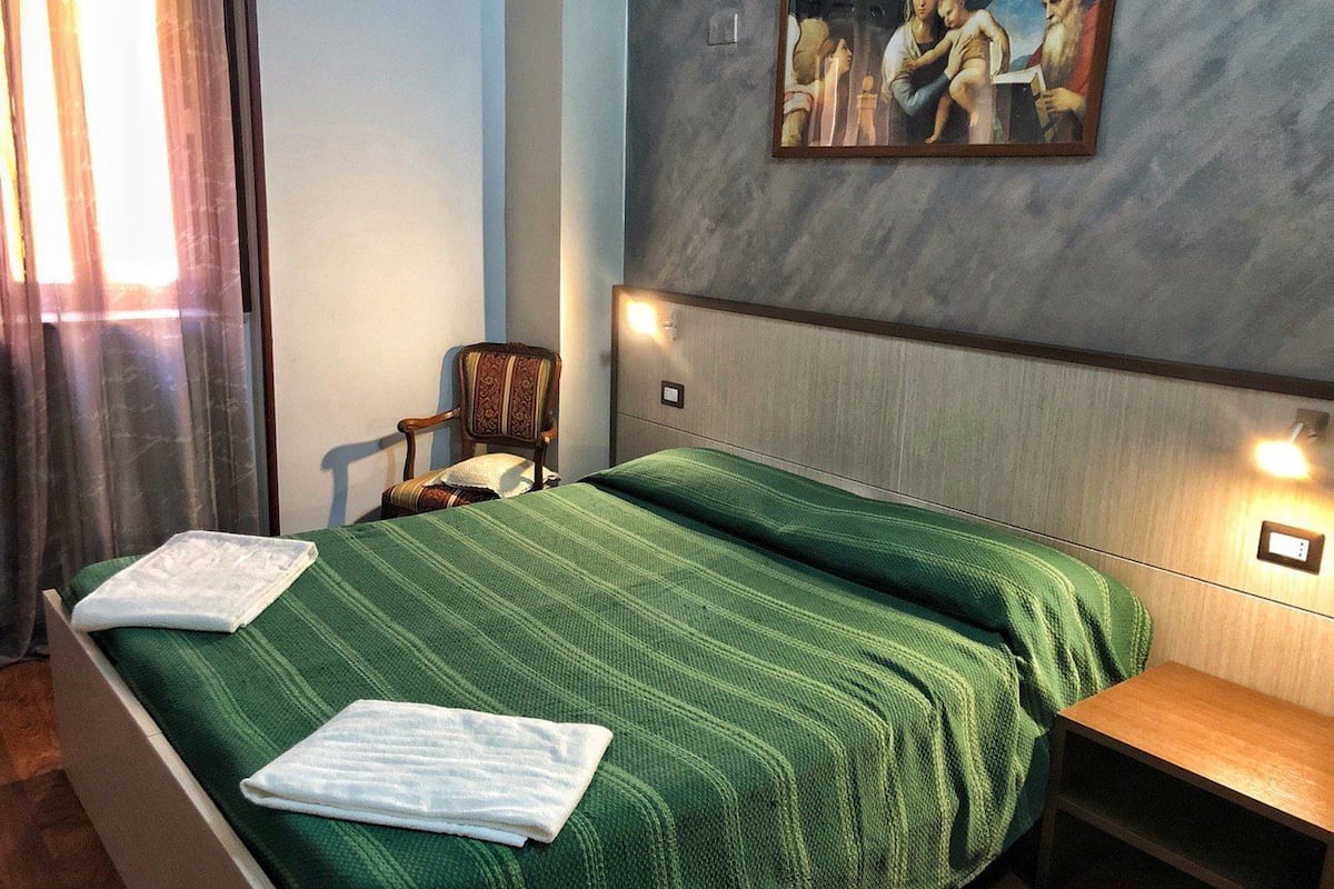 A hotel room with a large bed, a chair, a small table, and a painting on the wall.