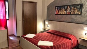 A hotel room with a wooden floor, a bed with a red striped bedspread, a painting on the wall, and a door. - Populus (Syracuse)
