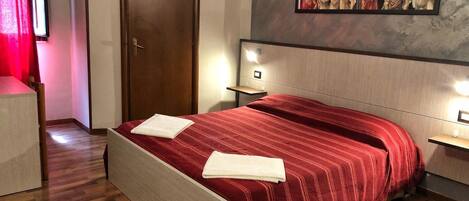 Una habitación de hotel con suelo de madera, una cama con colcha a rayas rojas, un cuadro en la pared y una puerta.