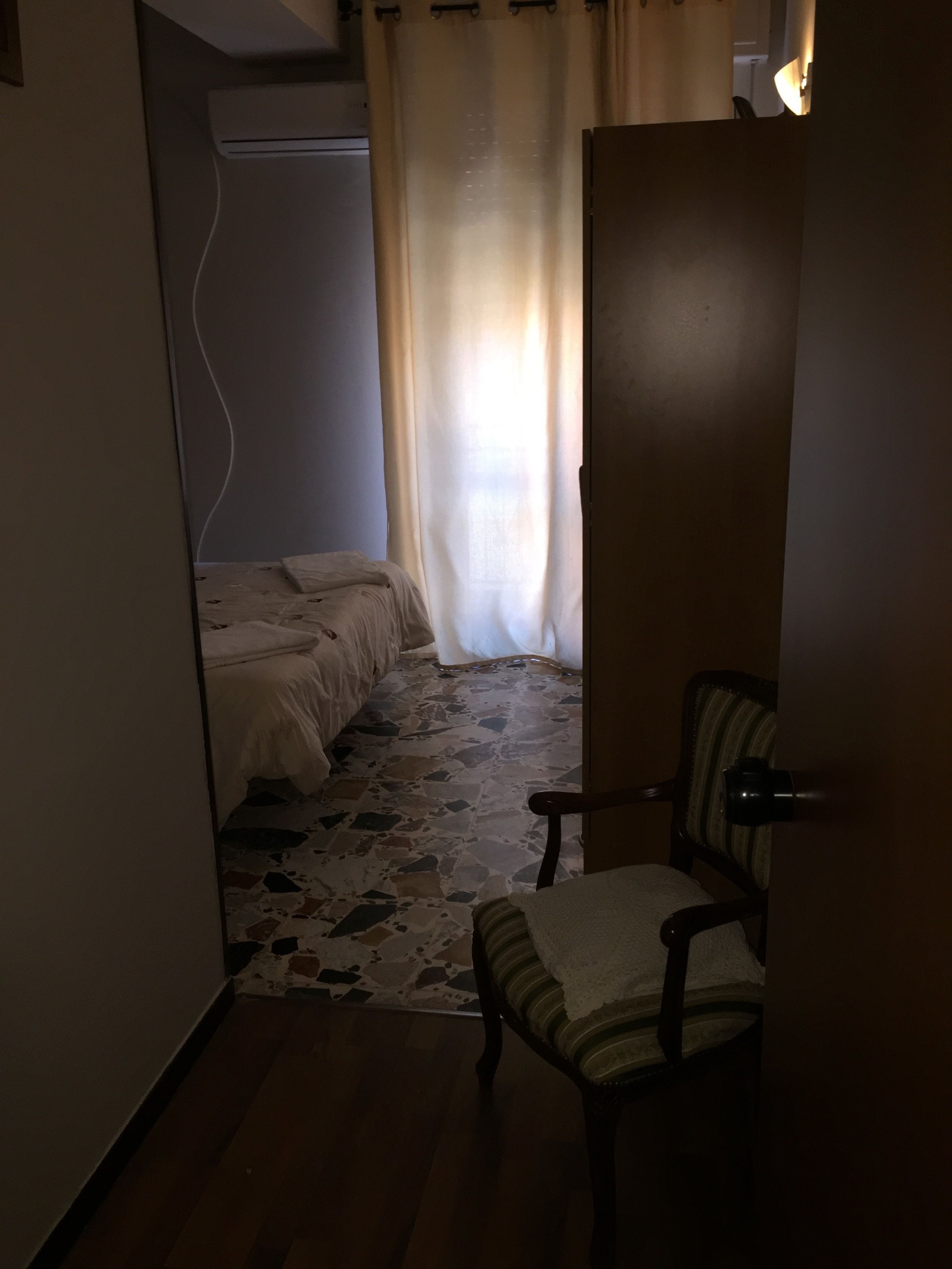 Een smalle gang met een bed, een stoel en een deur.