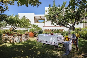 An outdoor seating area with a table set for two, surrounded by potted plants and a stone wall.