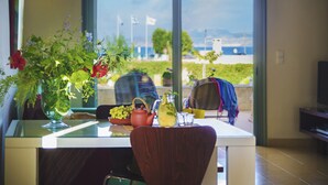 A dining area with a table set for two, a vase of flowers, a teapot, and a pitcher. A window provides a view of the outdoors. - Nereids (Sitia)