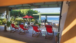 A covered outdoor seating area with red chairs and umbrellas, overlooking a beach. - Nereids (Sitia)