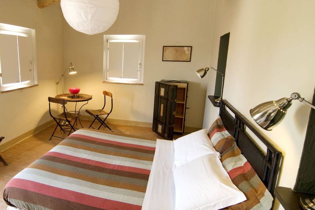 A bedroom with a bed, a desk, a chair, a lamp, and a wardrobe.