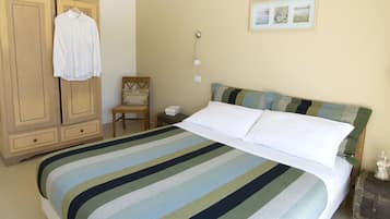 A bed with striped bedding, a wooden wardrobe, a chair, a bedside table with a lamp, and a framed picture on the wall.