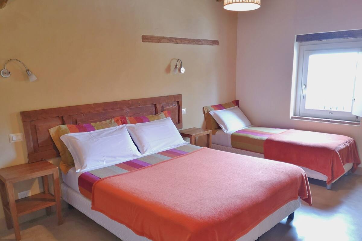 A hotel room with two beds, wooden headboards, bedside tables, a window, and a wall-mounted light fixture.