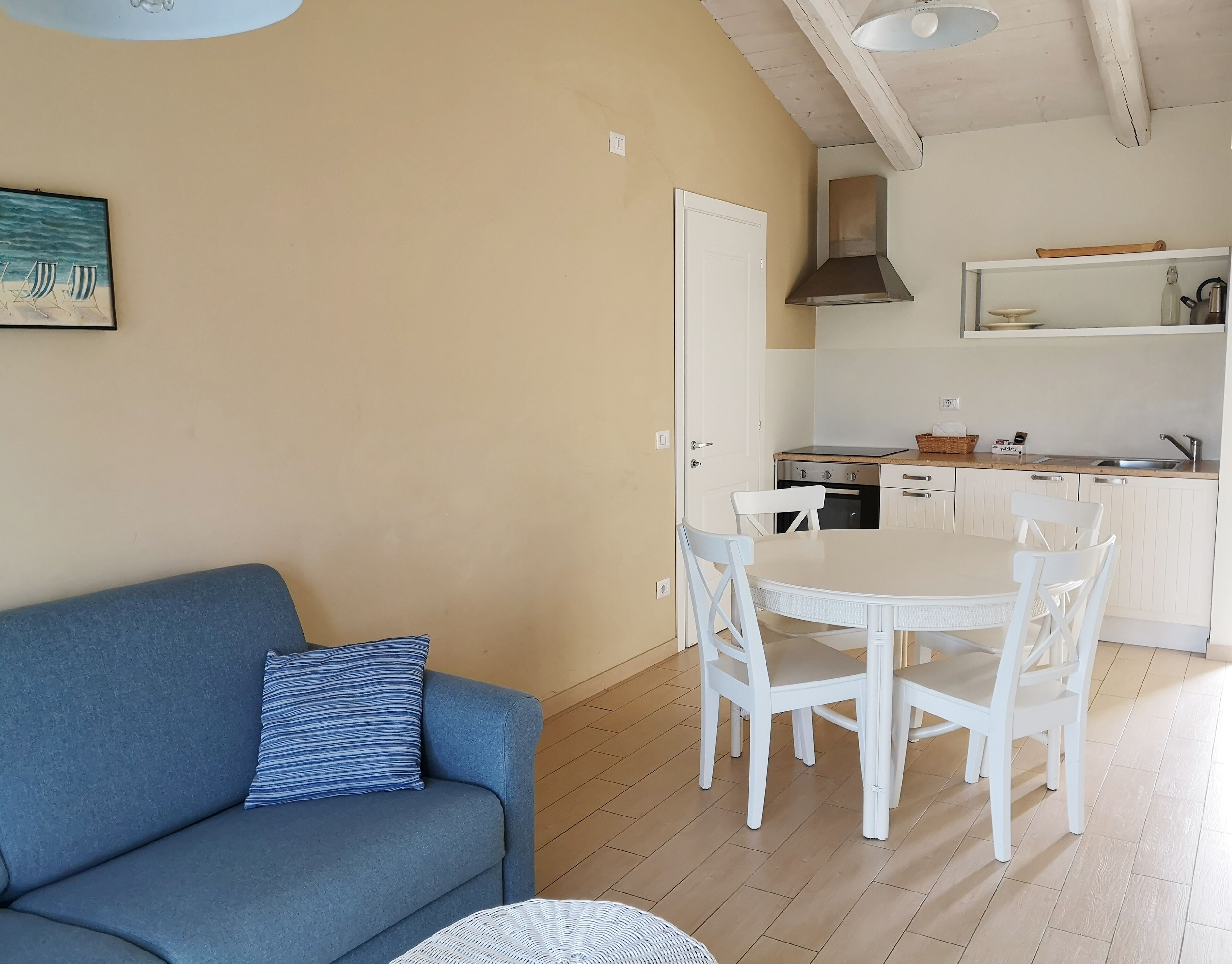 A compact living space with a blue sofa, a dining table with white chairs, a kitchen area with white cabinets, and a ceiling fan.