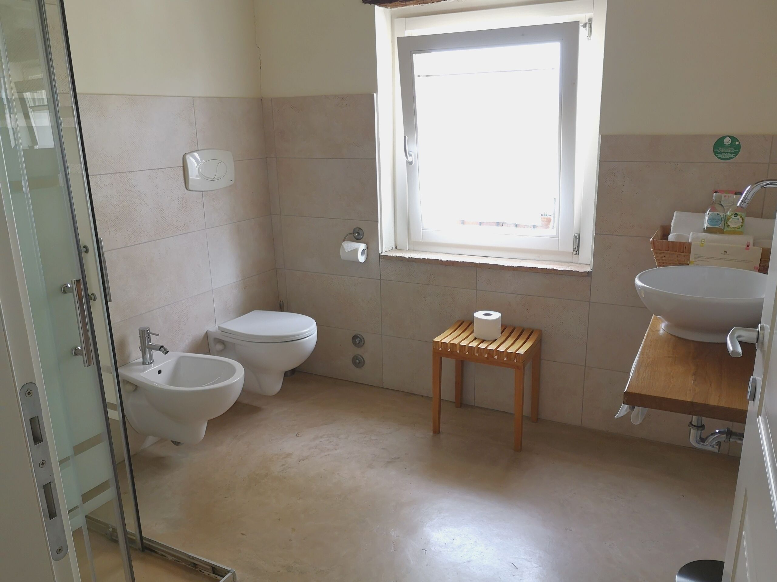 Un bagno con il water, un bidet, un lavandino e un piccolo sgabello di legno.