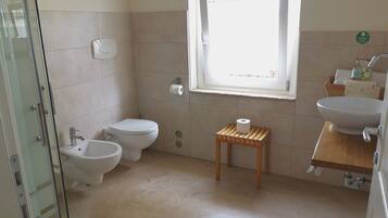 Un bagno con il water, un bidet, un lavandino e un piccolo sgabello di legno.
