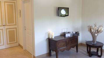 A hallway with a wooden console table, a small round table with a vase, and a mounted television.