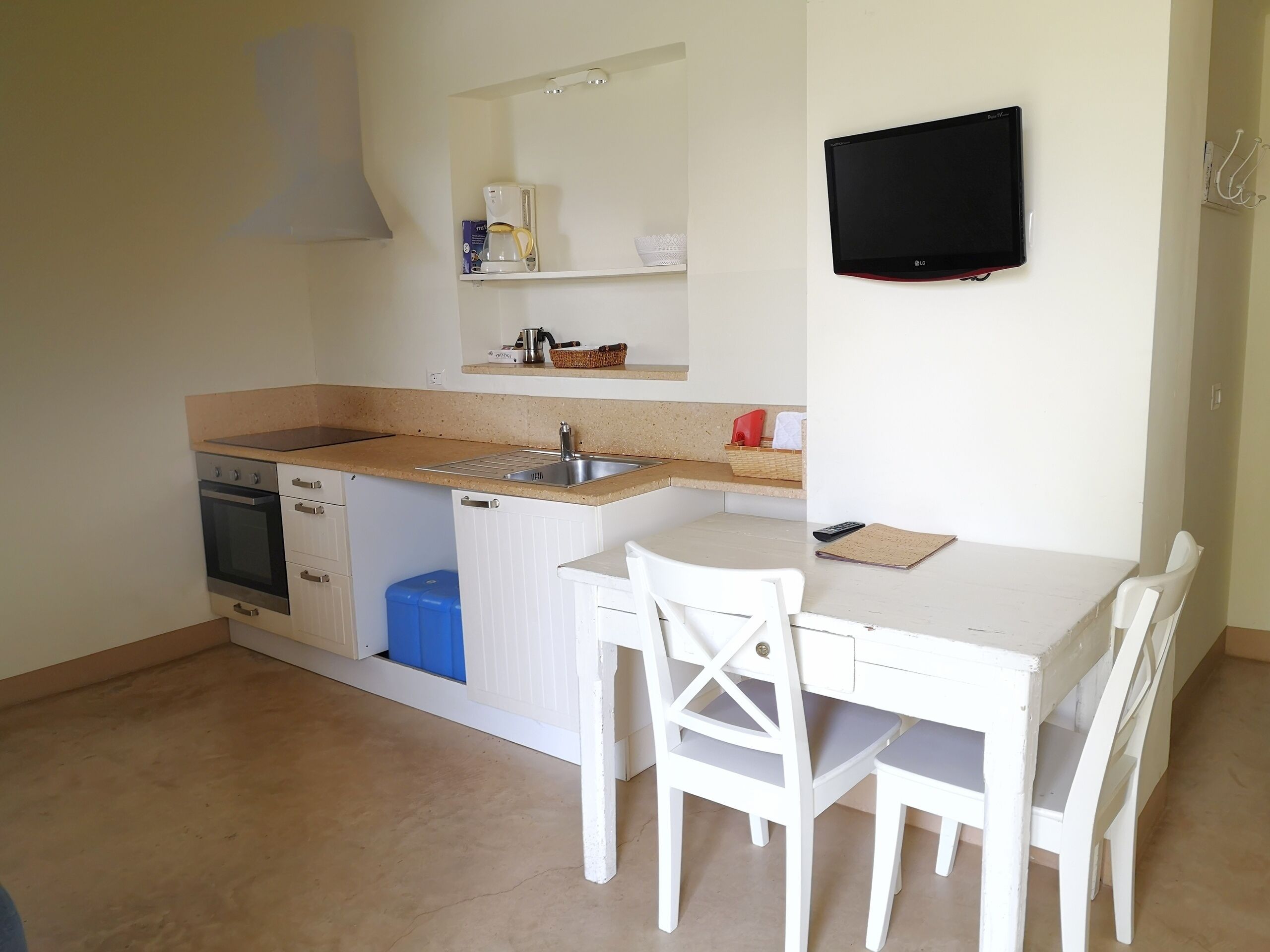 Een compacte keuken met een spoelbak, kookplaat en vaatwasser, een eettafeltje met stoelen en een flatscreen televisie aan de muur.