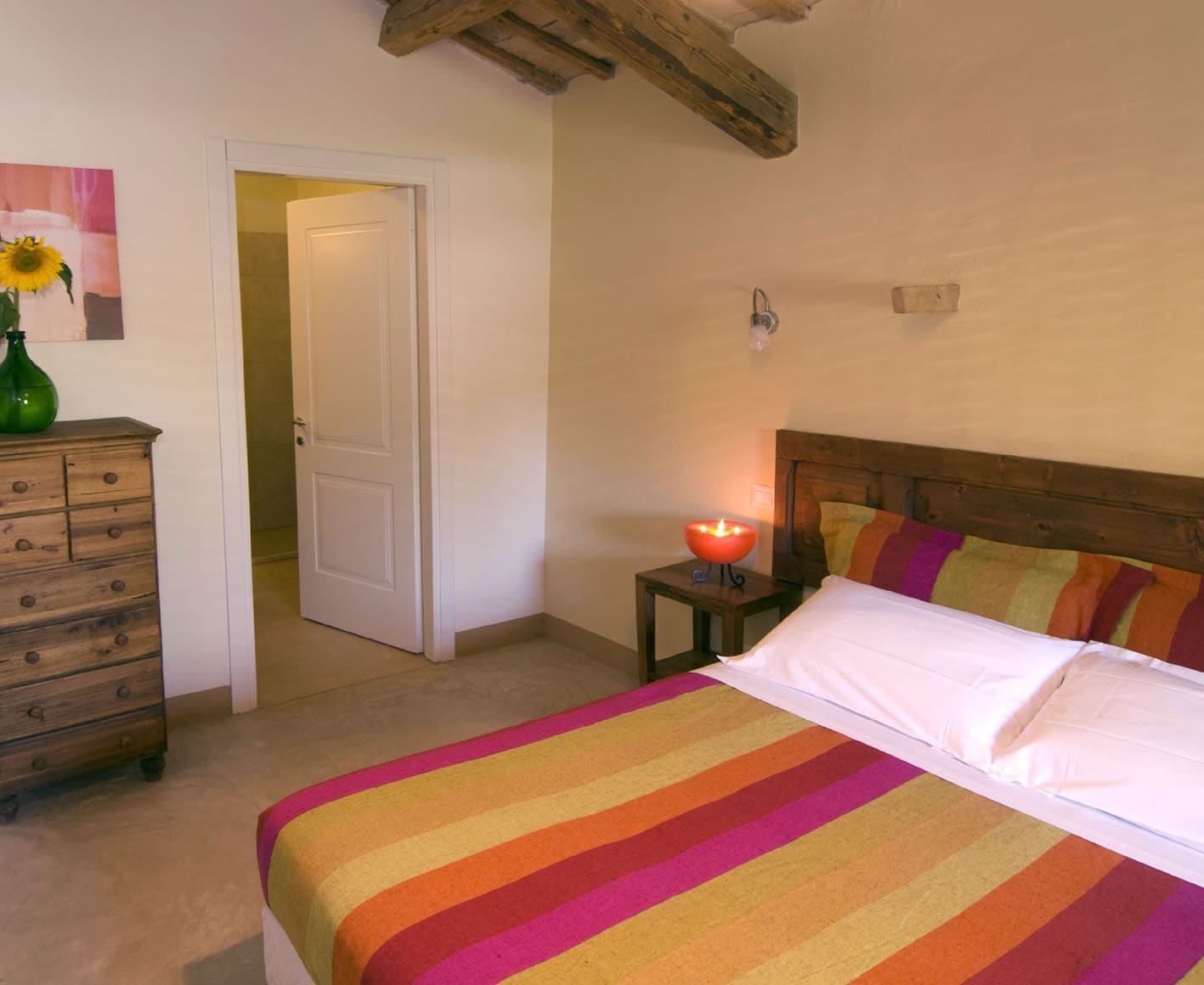 A bedroom with a bed, a dresser, a nightstand with a candle, and a door leading to another room.