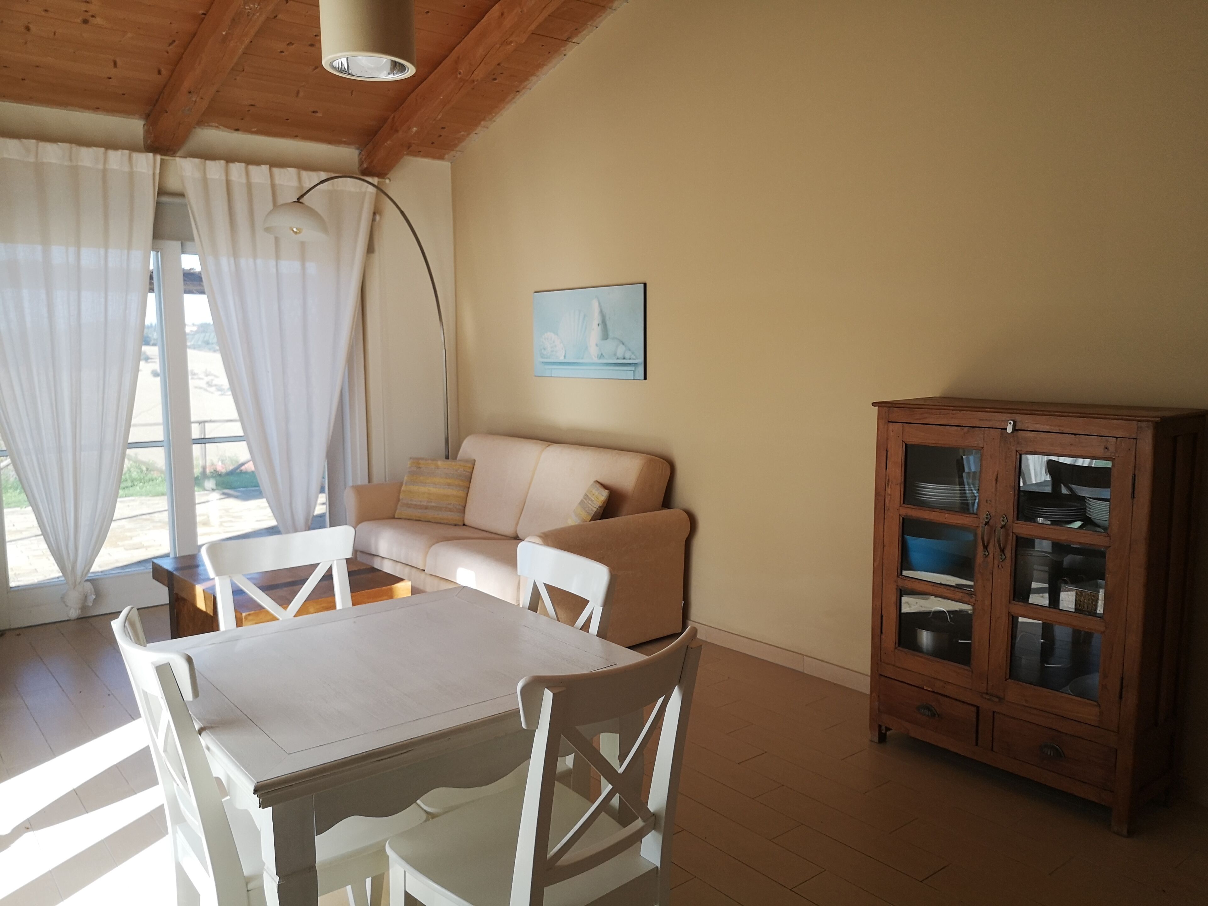 Un comedor con una mesa y sillas de madera, un sofá beige y un aparador con puertas de cristal.