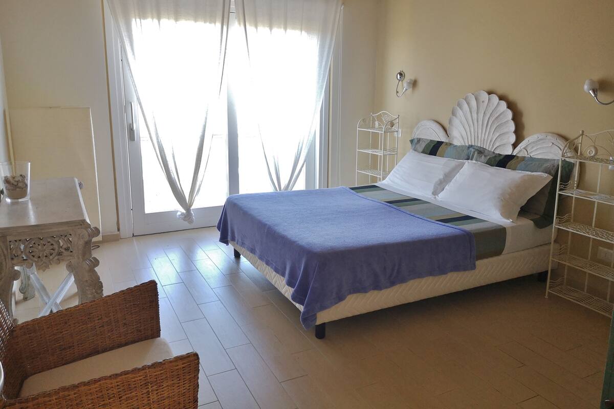 A bedroom with a bed, a chair, a nightstand, and a window with curtains.