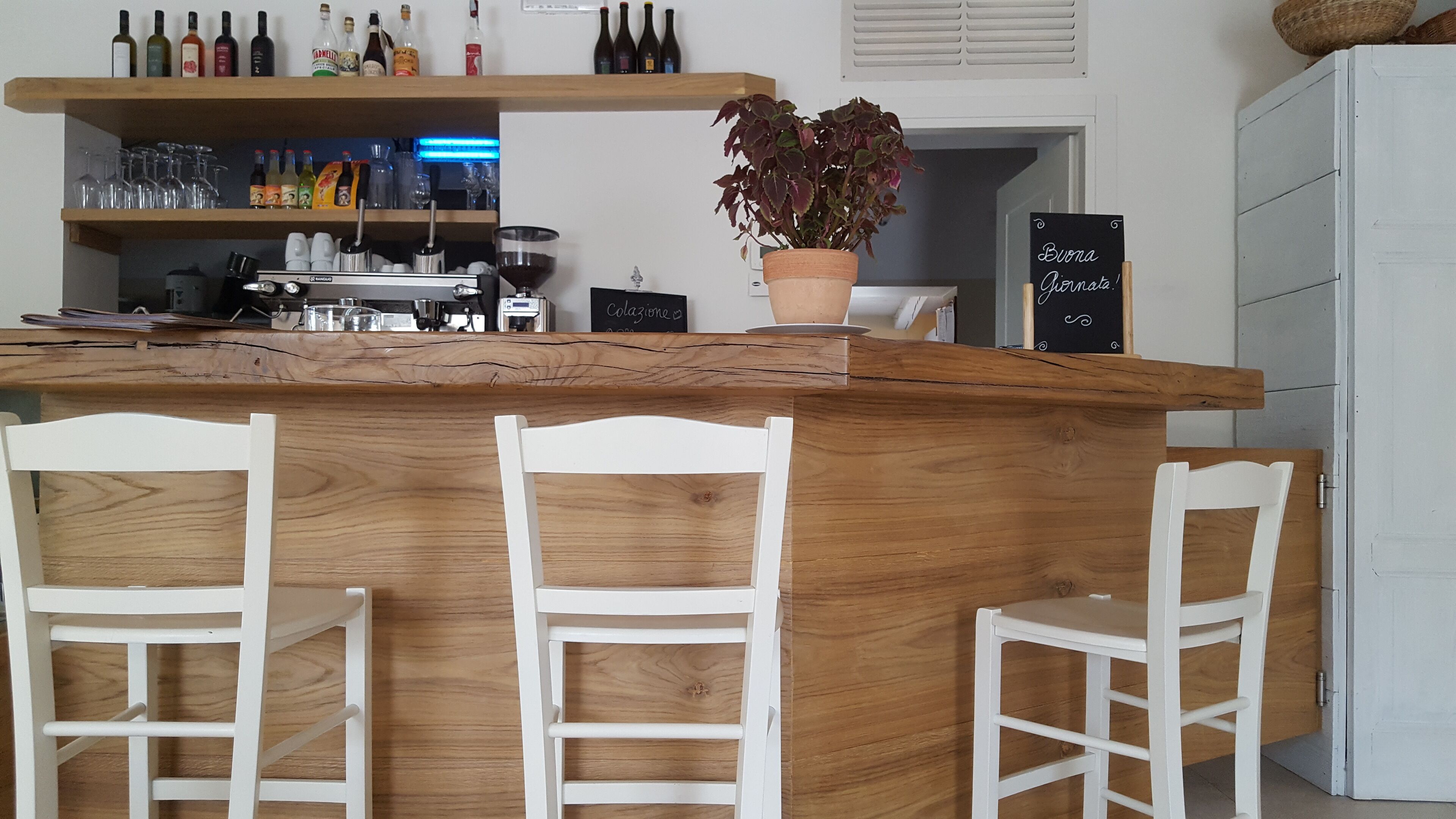 Eine Bar mit weißen Stühlen, einer Holztheke und Regalen voller Flaschen und Gläsern.
