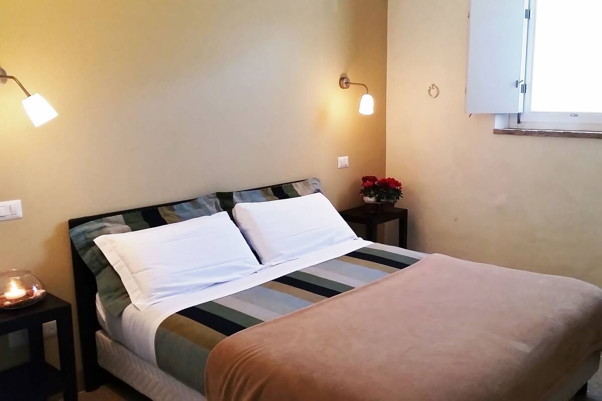 A bed with a striped bedspread, a bedside table with a lamp, and a window with a view of the outside.