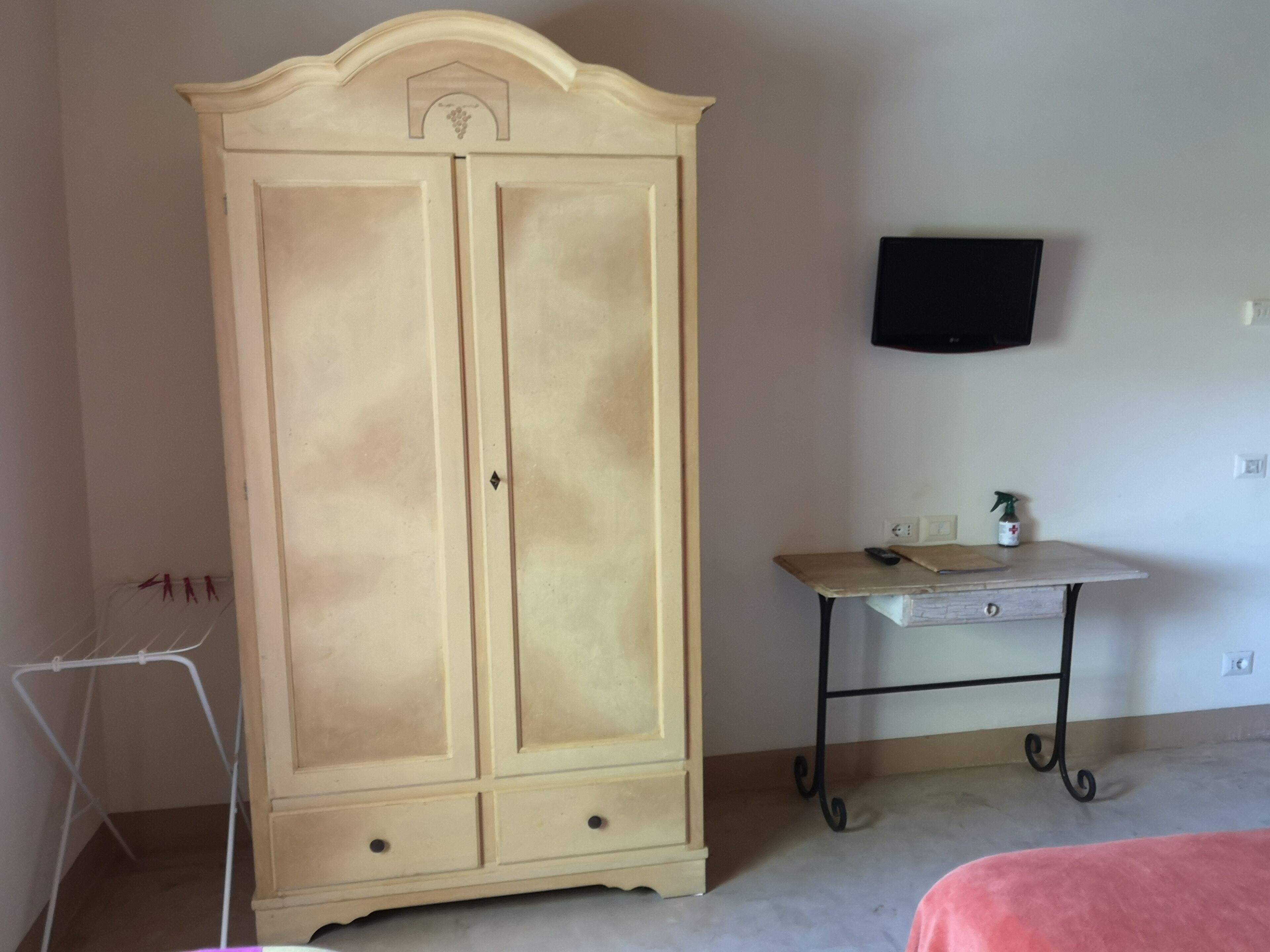 A room with a large wardrobe, a small table with a spray bottle, and a TV mounted on the wall.