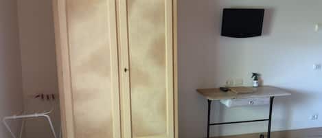A room with a large wardrobe, a small table with a spray bottle, and a TV mounted on the wall.