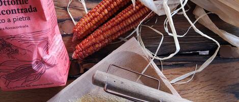 A wooden surface with corn cobs, a metal sieve, and a pink bag with text.
