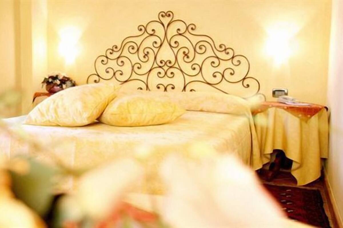 A bed with a decorative headboard, a bedside table with a lamp, and a floral arrangement.