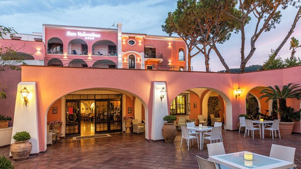 A hotel with a pink facade, outdoor seating area, and a sign reading "San Valentino". - Hotel San Valentino (Ischia)